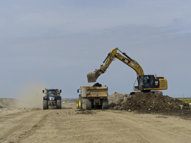 An excavator loads a dump truck on a dusty construction site in Noord-Holland, Nederland.