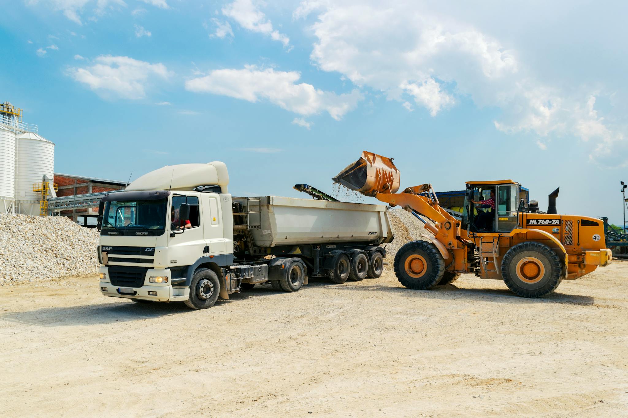 Home Excavator loading materials into a heavy-duty truck at a sunny construction site.