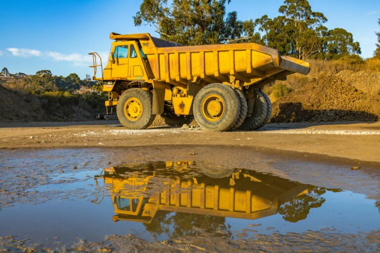 Yellow dump truck with reflection in water at a mining site, exhibiting industry machinery.